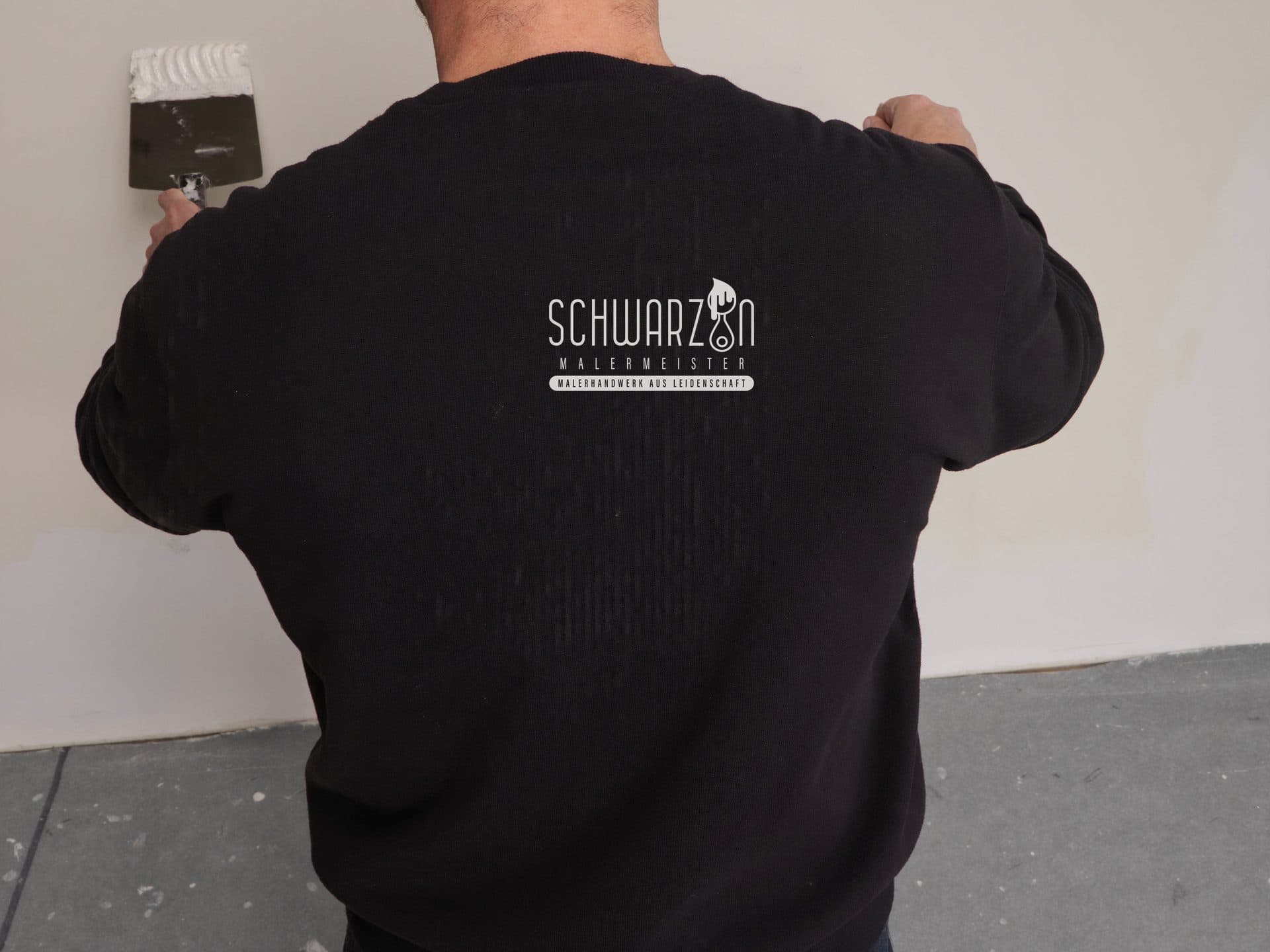 Maler im Schwarzin-Arbeitspullover bei präziser Spachtelarbeit